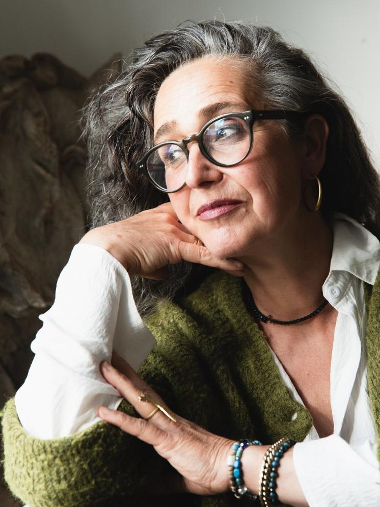 Christiane Churchill-Ley in a green cardigan on a woodland path bordered by wild white roses and greenery.